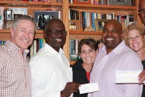 Five people smiling at camera holding documents in front of home bookshelf