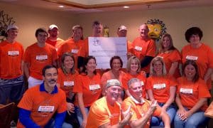 Large group wearing orange DFW Smiles shirts posing together indoors for team photo.
