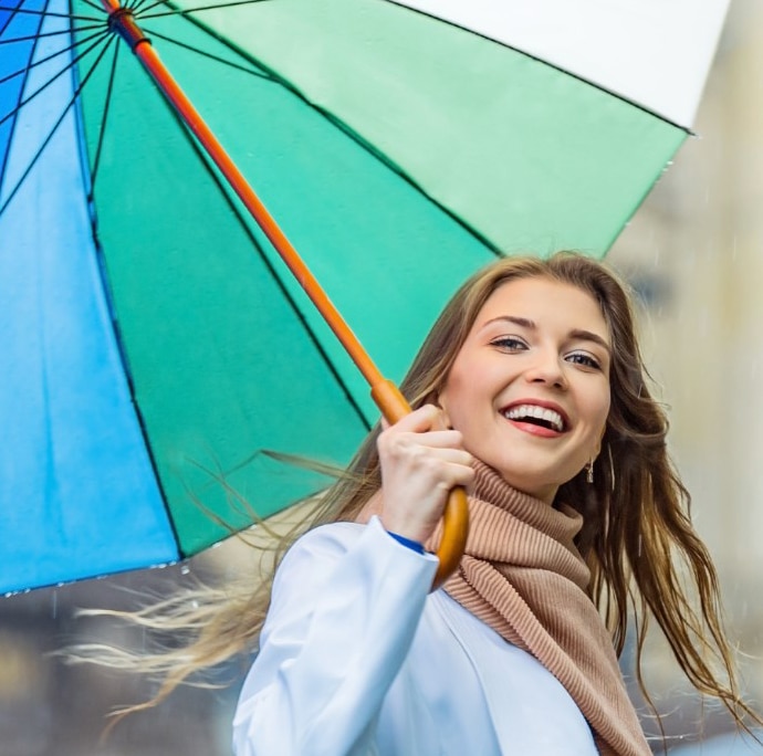 Woman holding colorful umbrella, smiling outdoors in casual attire.
