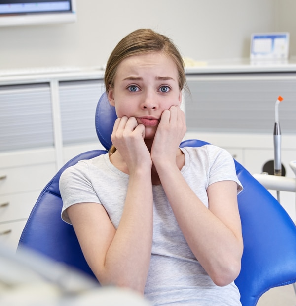 Anxious young woman in dental chair biting nails at dentist office.