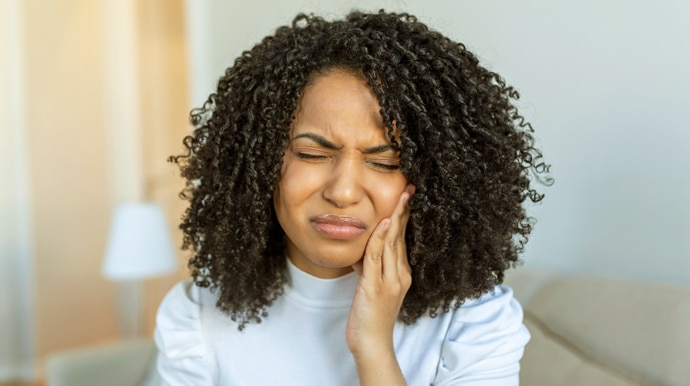 Woman with curly hair touching cheek in discomfort, suggesting dental pain or sensitivity in clinical setting.