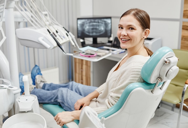 Smiling female patient relaxed in dental chair during examination at modern dental office.