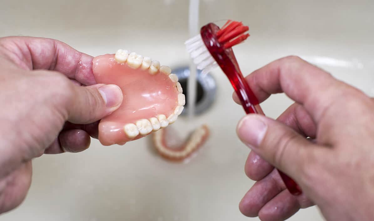 Hands holding dental model and red instrument demonstrating dental procedure in clinical setting.