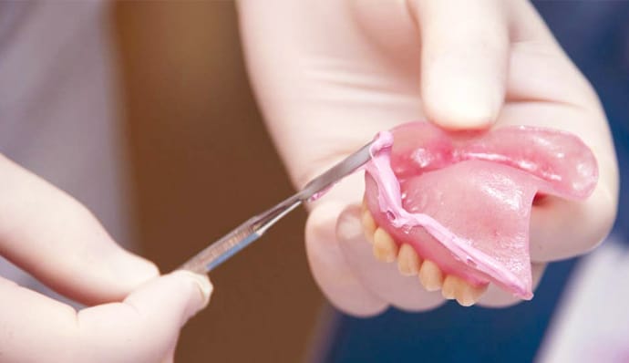 Dentist holding dentures while patient examines them during consultation.