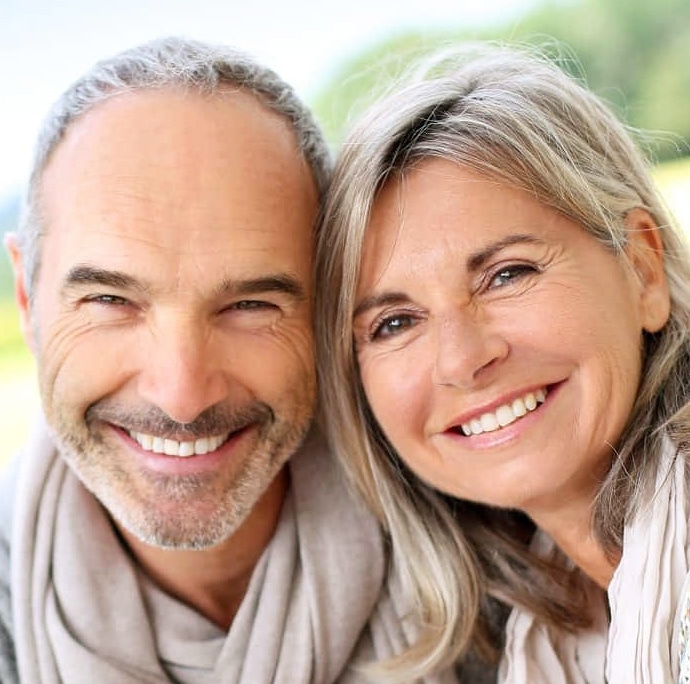 Middle-aged couple smiling at camera outdoors in natural daylight setting.
