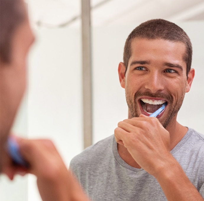 Man brushing teeth while looking in bathroom mirror, smiling.