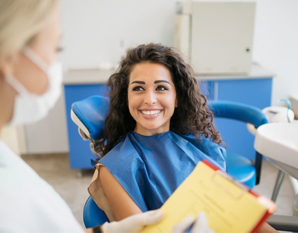 Patient in dental bib smiles at dentist in modern dental office treatment room.