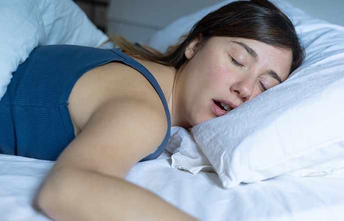 Woman sleeping peacefully on white pillow and blue bedding in bedroom setting.