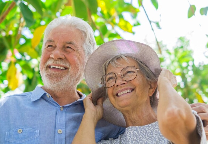 Happy senior couple smiling outdoors under tree foliage on sunny day.