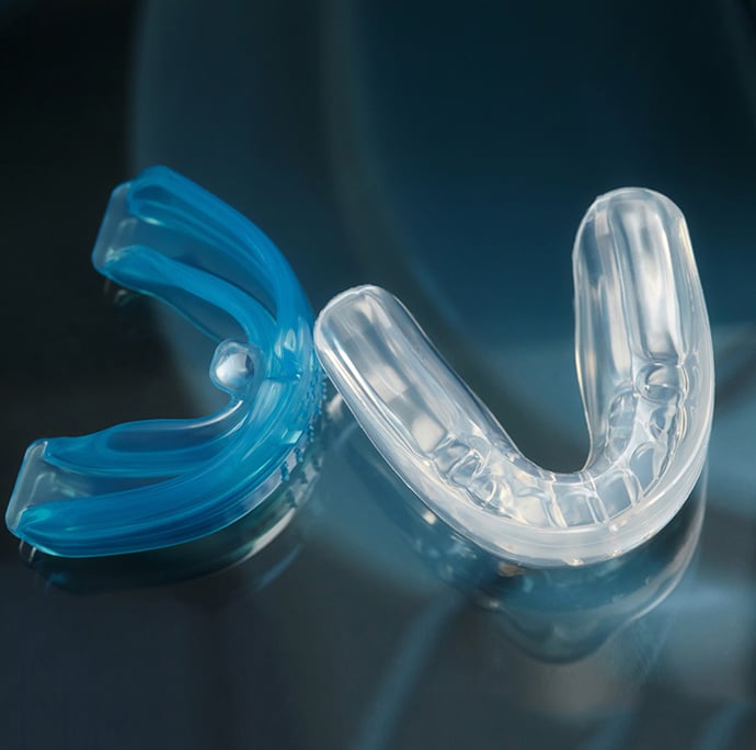 Two custom dental mouth guards, one blue and one clear, displayed on dark surface.